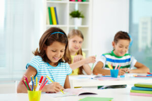 Portrait of lovely girl drawing at workplace with schoolmates on background